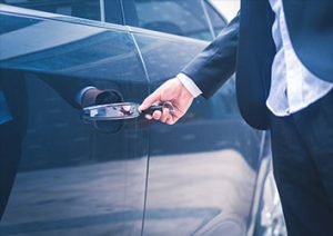 A man in a suit is opening the door of his car.