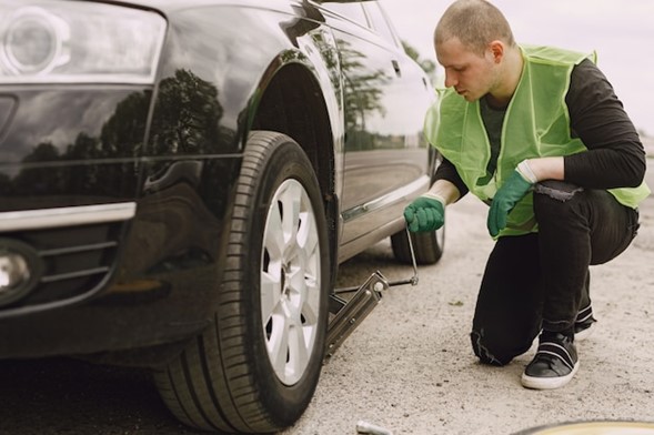 A man in green jacket working on car tire.