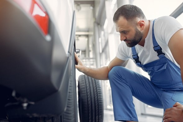 A man in blue pants and white shirt fixing a car.