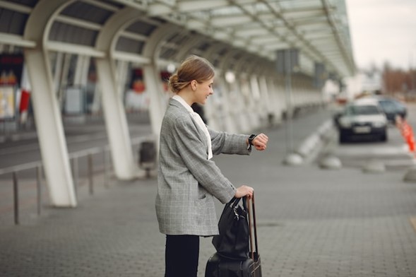 A woman in grey jacket holding black bag near wall.